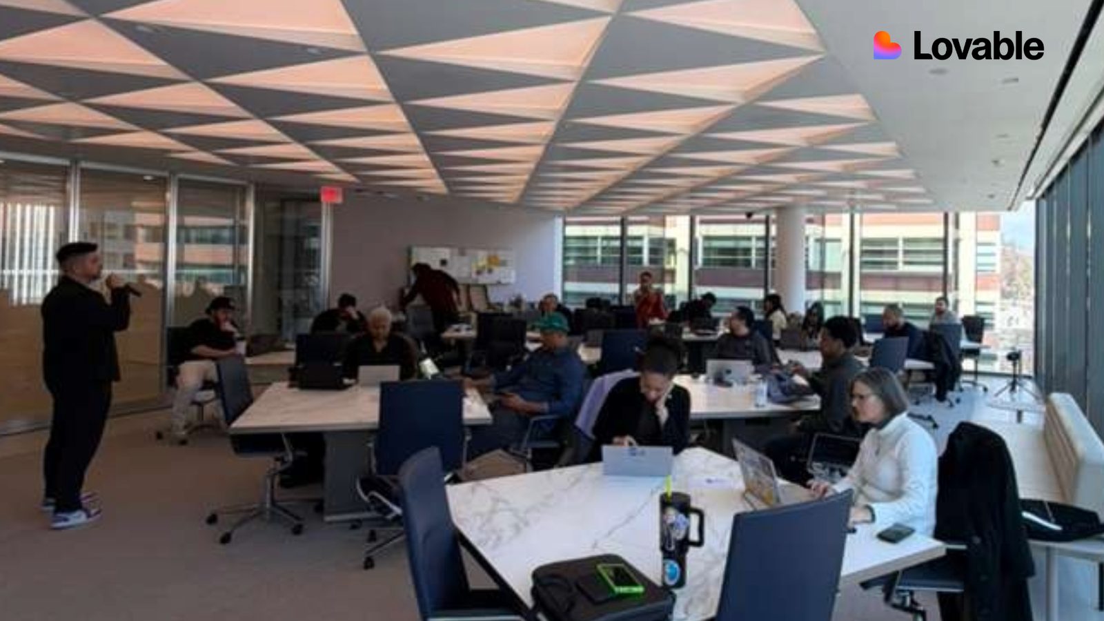 Attendees working on laptops around white tables during a workshop