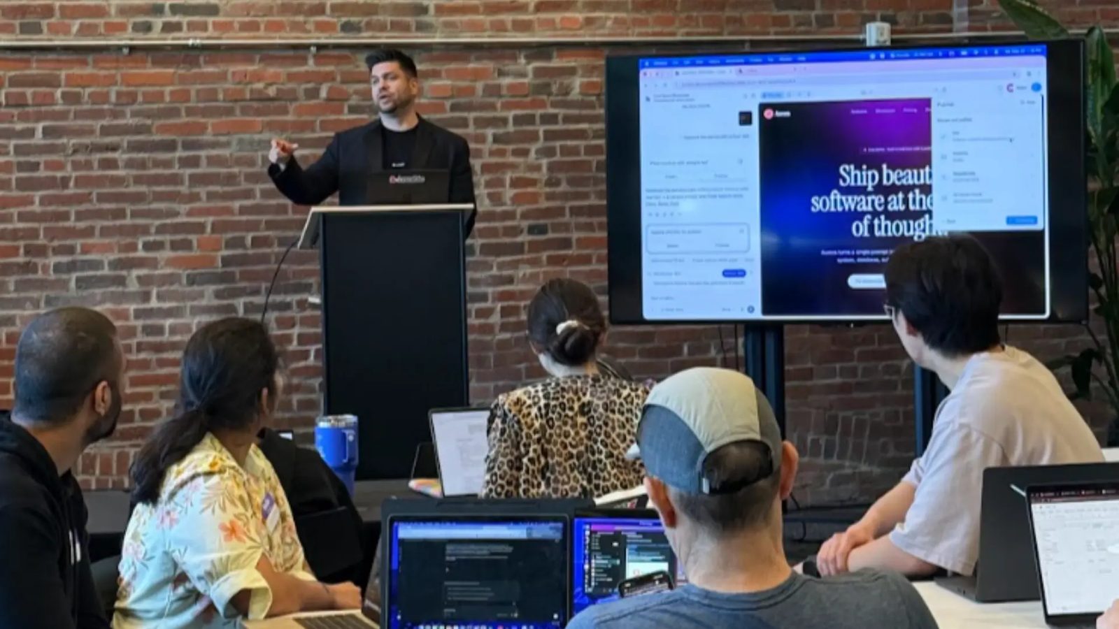 Presenter at a podium beside a large screen showing a web design interface